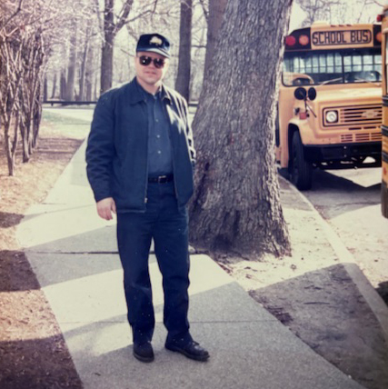 Michael standing on a sidewalk in front of a school bus when he was a bus driver